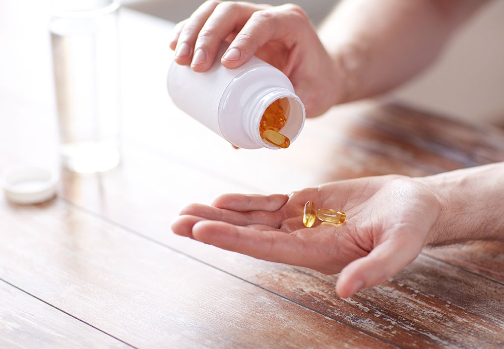 Close up of man with glass of water pouring supplement capsules from jar to hand