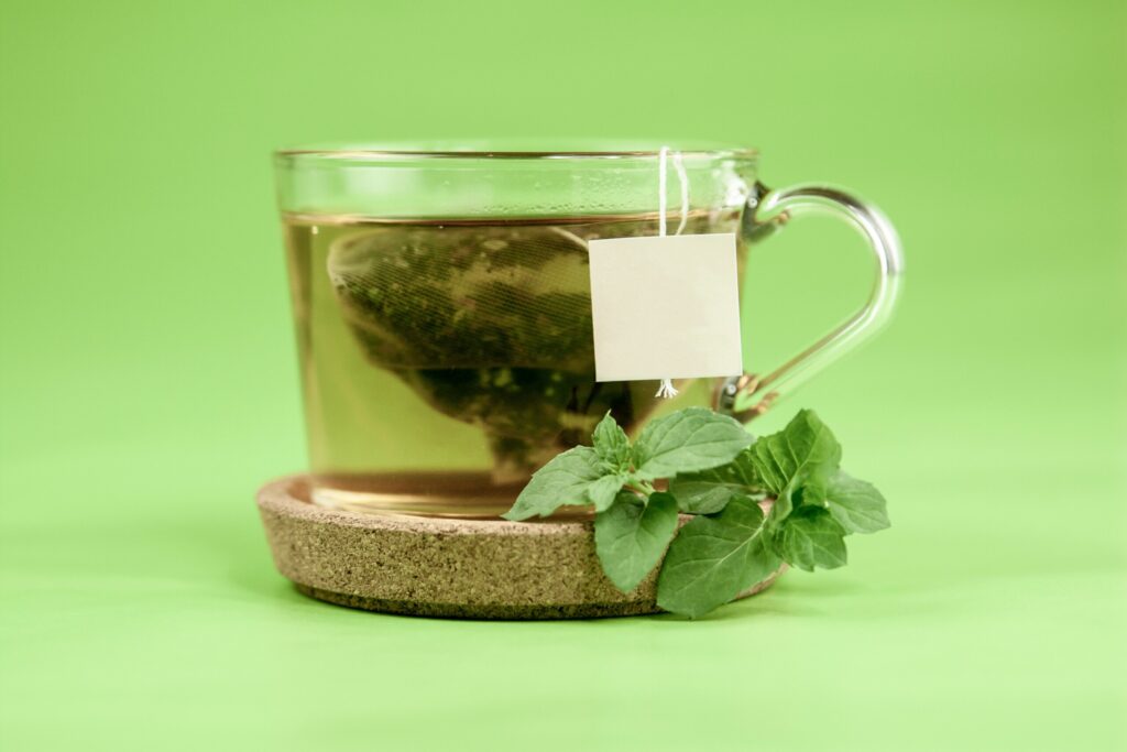 A mug of green tea with a tea bag and mint leaves 